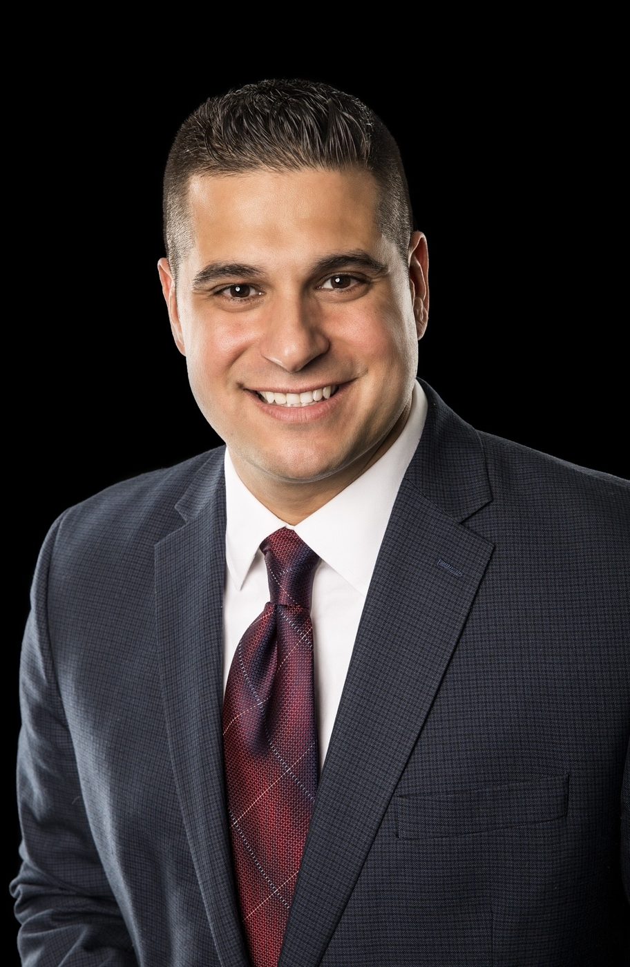 Headshot of a smiling man in a navy suit and red tie